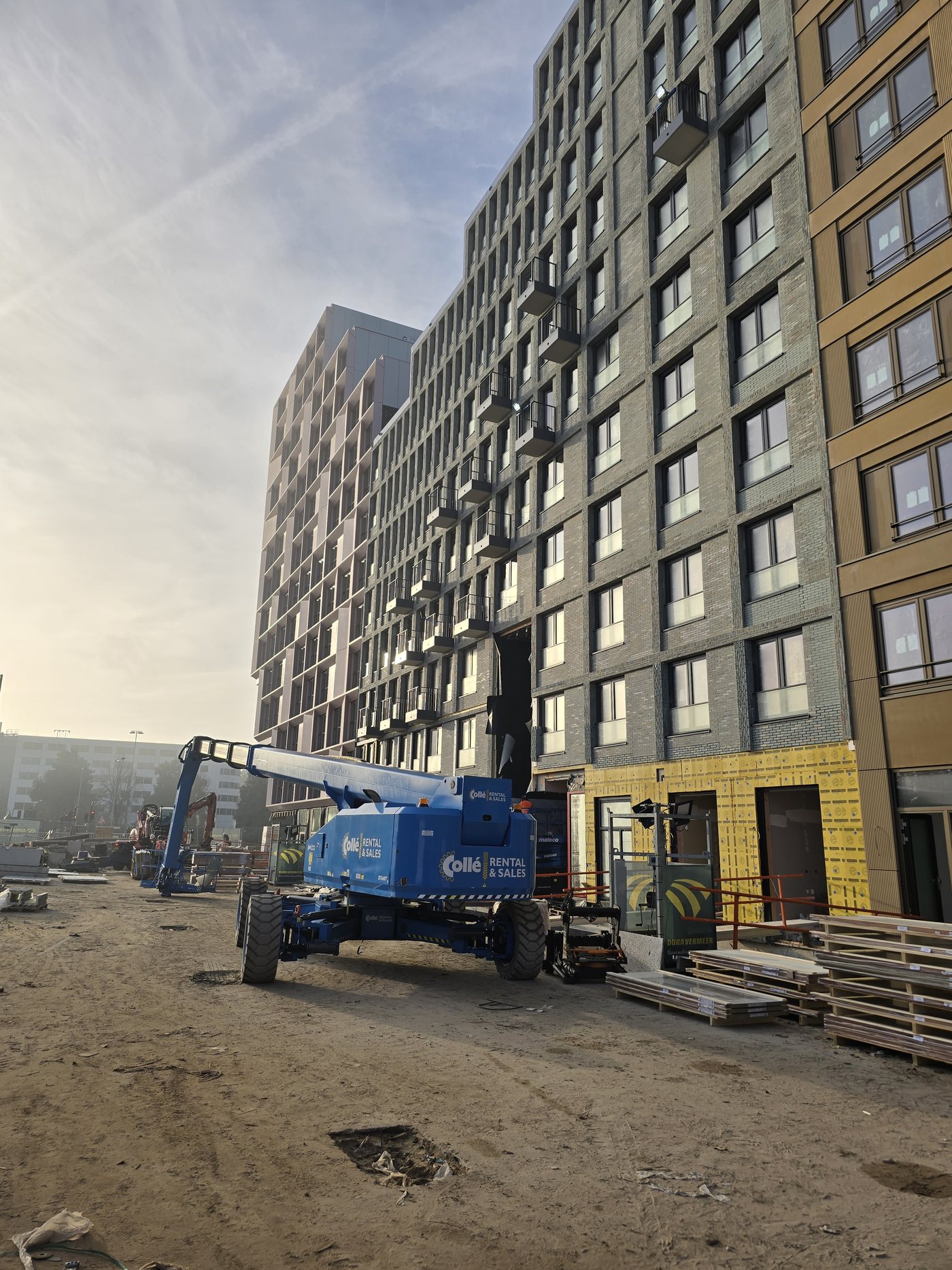 Gevel van een groot woongebouw in aanbouw, met een hoogwerker op de bouwplaats