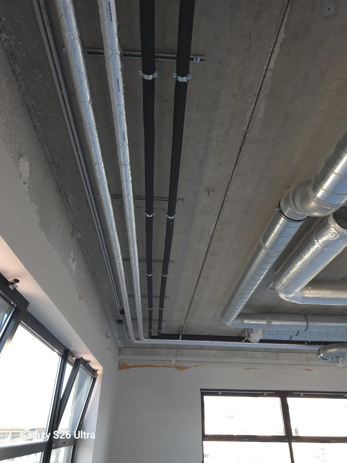 Ventilation ducts and pipework on the ceiling, with daylight through the windows